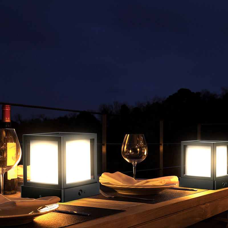 Dining table setup with wine glasses, bottle, and lit lanterns at night.